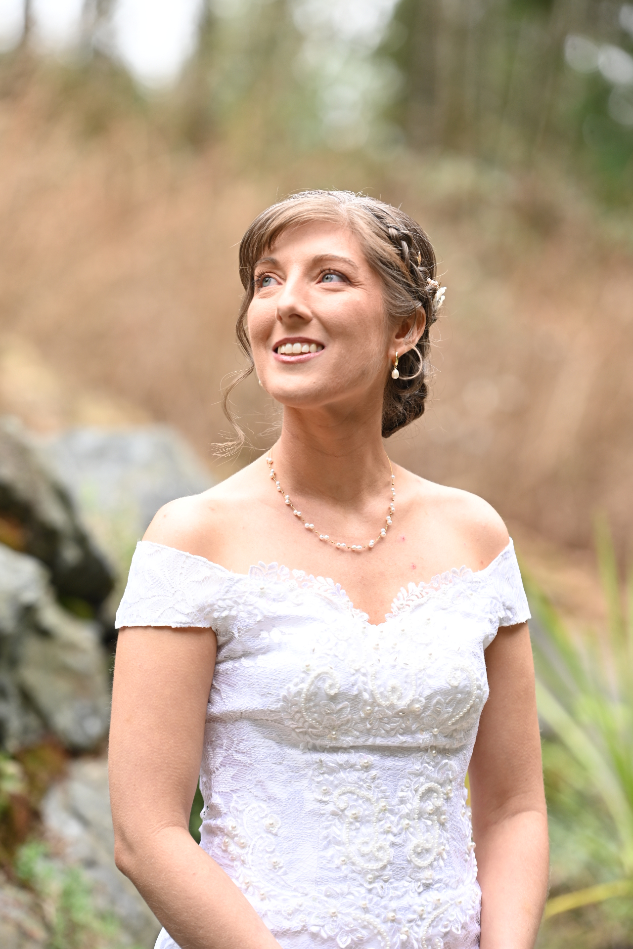 Bride smiling in lace gown beside mossy rocks